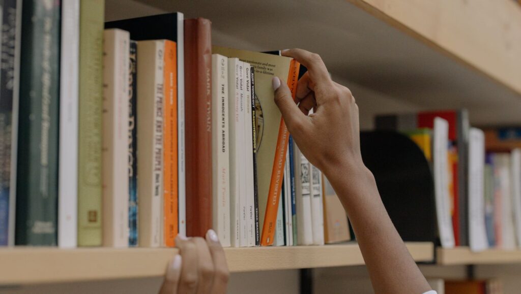 Hands reaching for and selecting a book from a bookshelf, symbolizing access to educational resources, research, and learning.