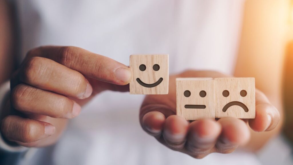 A hand holding wooden blocks displaying happy, neutral, and sad emotions, symbolizing social-emotional learning and understanding feelings.