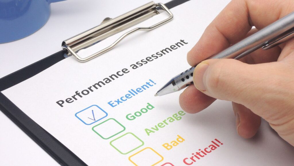 A hand holding a pen checking 'Excellent!' on a performance assessment form, symbolizing self-evaluation and growth.
